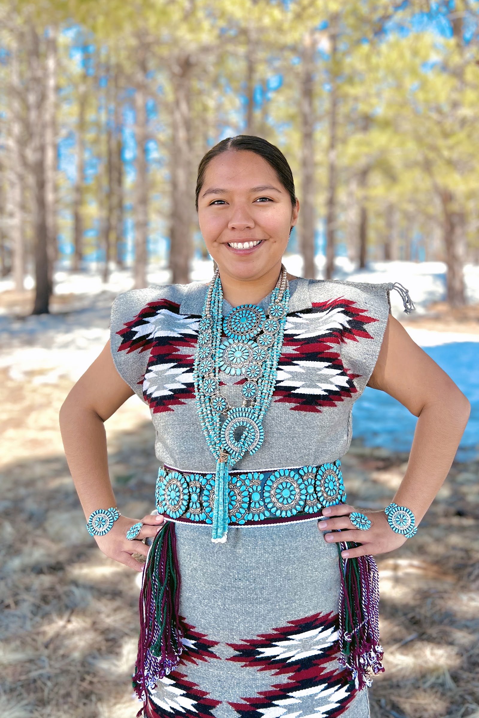 Sarah Chatter wearing a traditional Native American dress and turquoise jewelry with trees in the background.