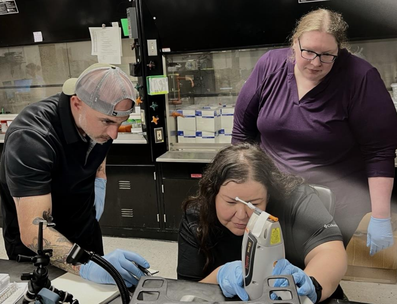 Mike Anastario (left) and Courtney Roper (right) train Diedre’ Goodluck to assess syringes using a portable x-ray fluorescence device.