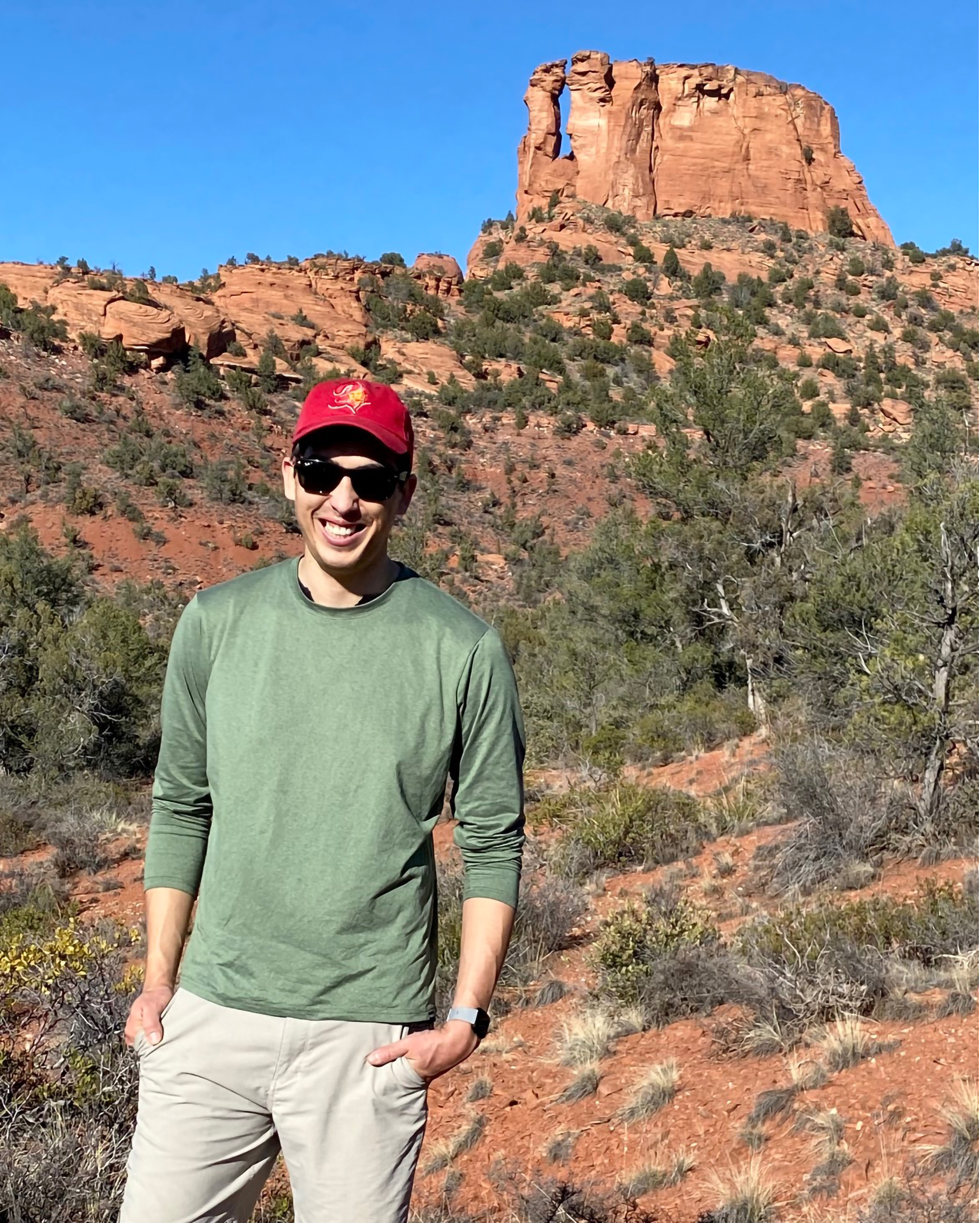 Skyler Bordeaux standing in front of a rock formation wearing a green shirt, red hat, and khaki pants.