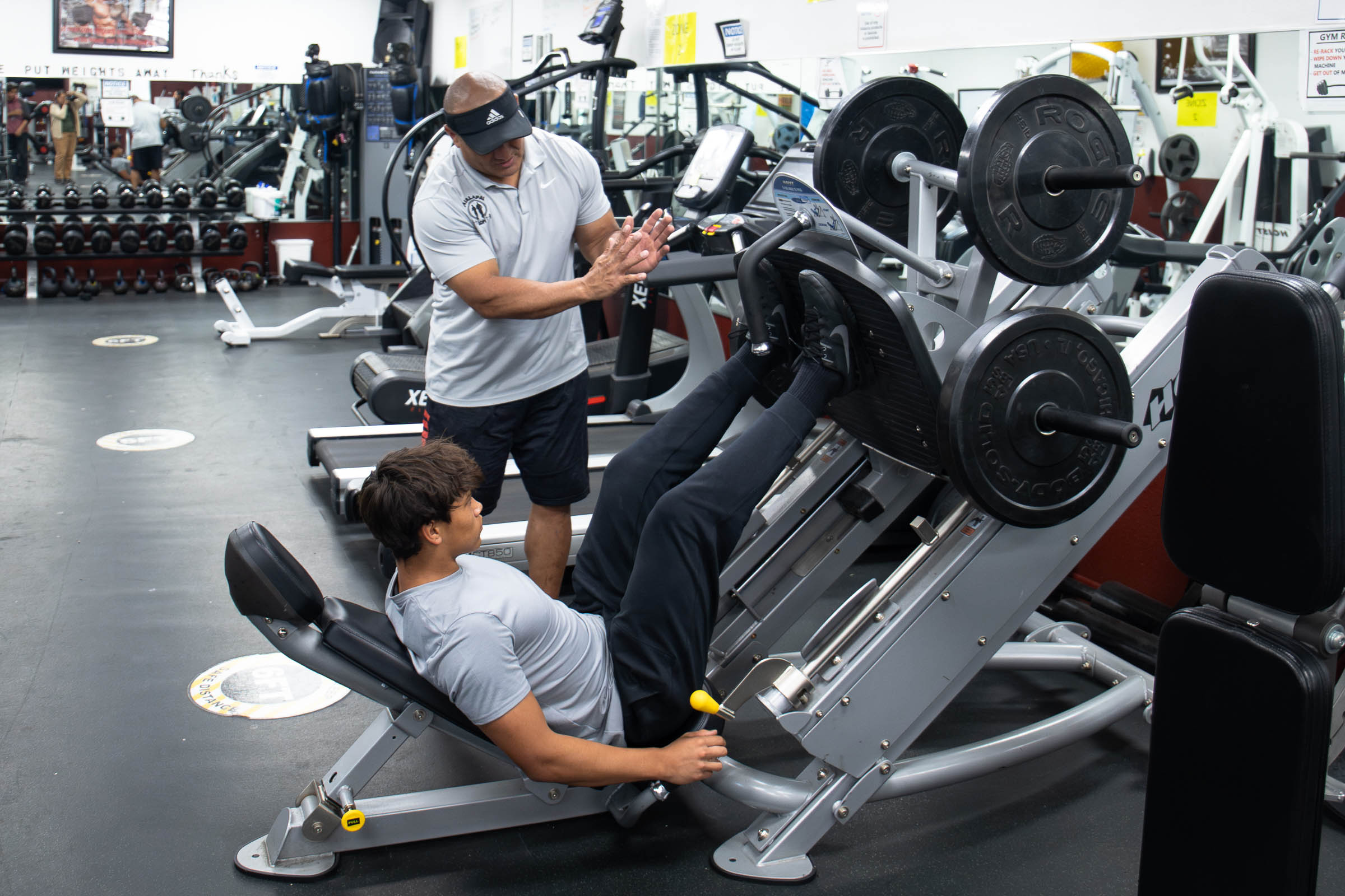 Male student doing leg presses with trainer.