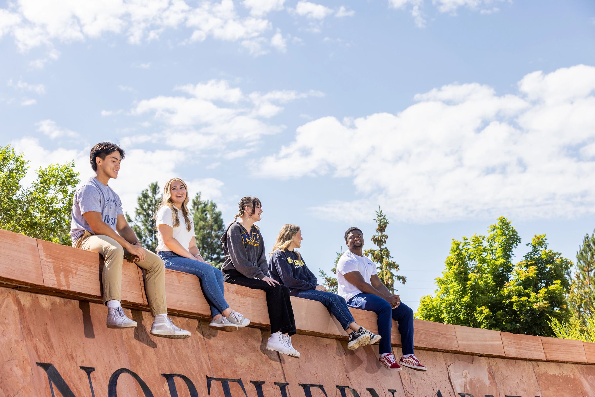 Five students sitting on the N A U welcome sign.