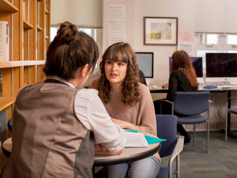 Two students talking to one another at a table.