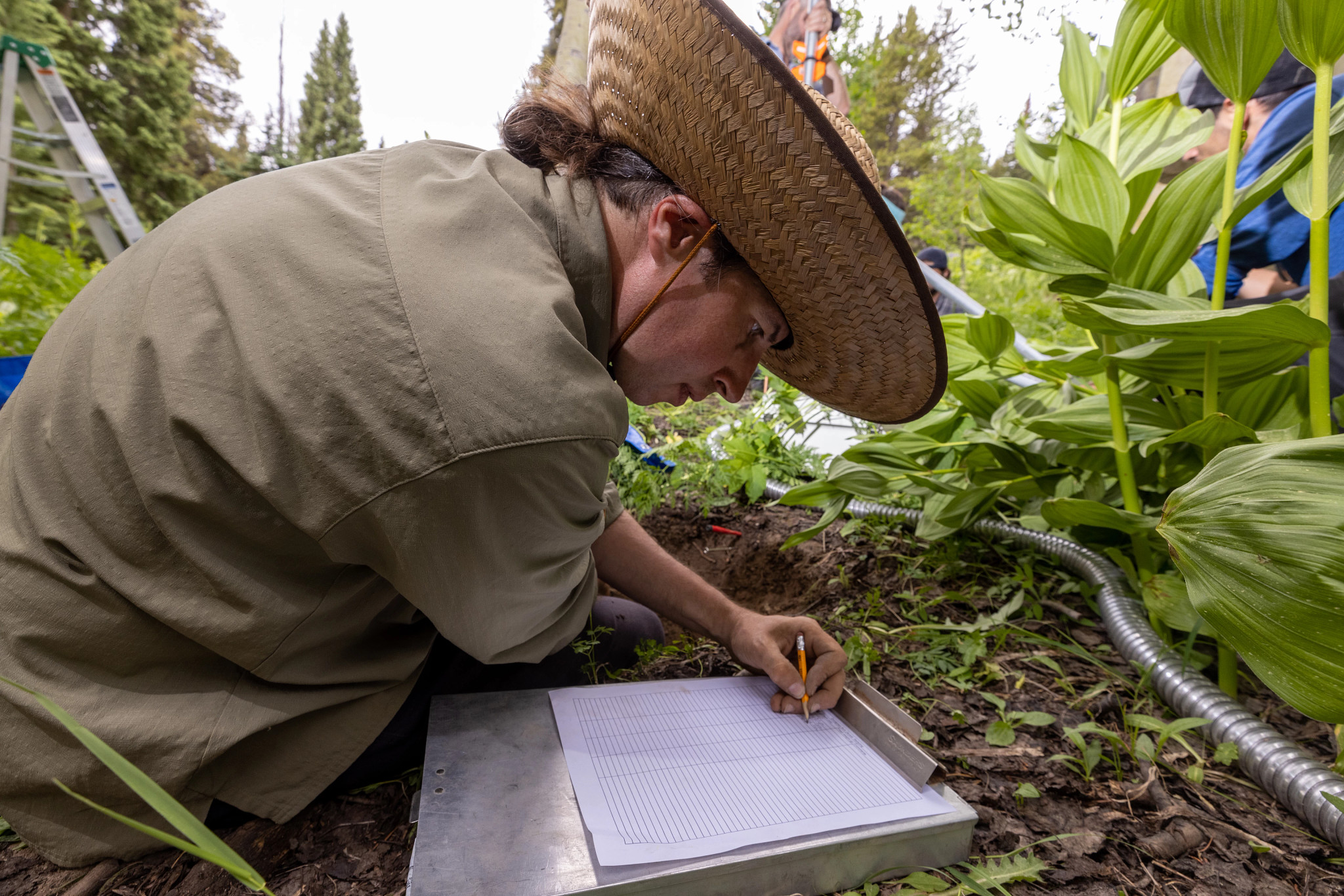 Student taking notes for an outdoor project on paper.