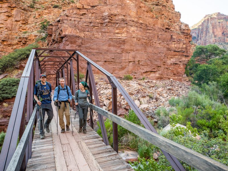 Three people walking through a bridge in the grand canyon.