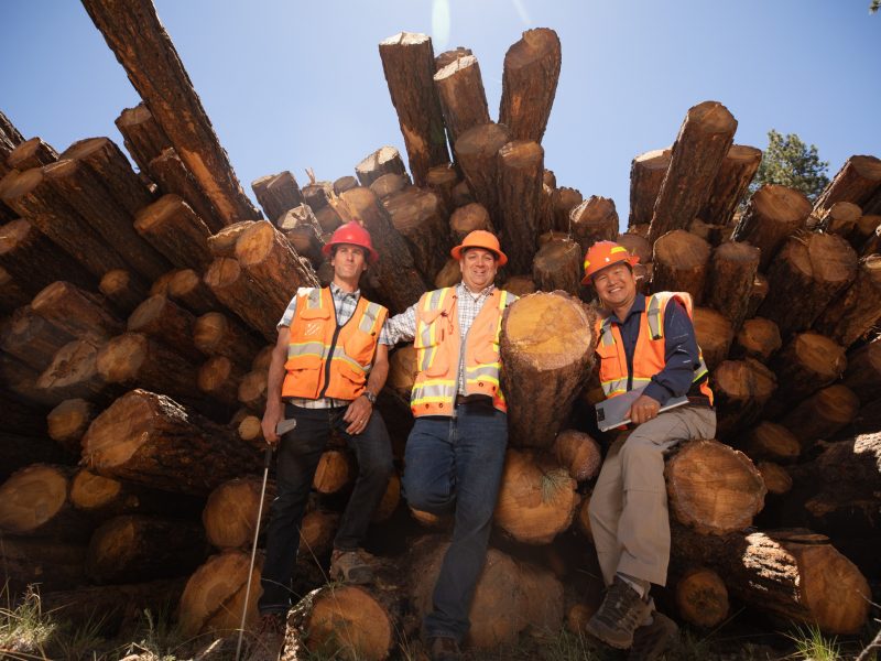 Three people sitting on lumber.