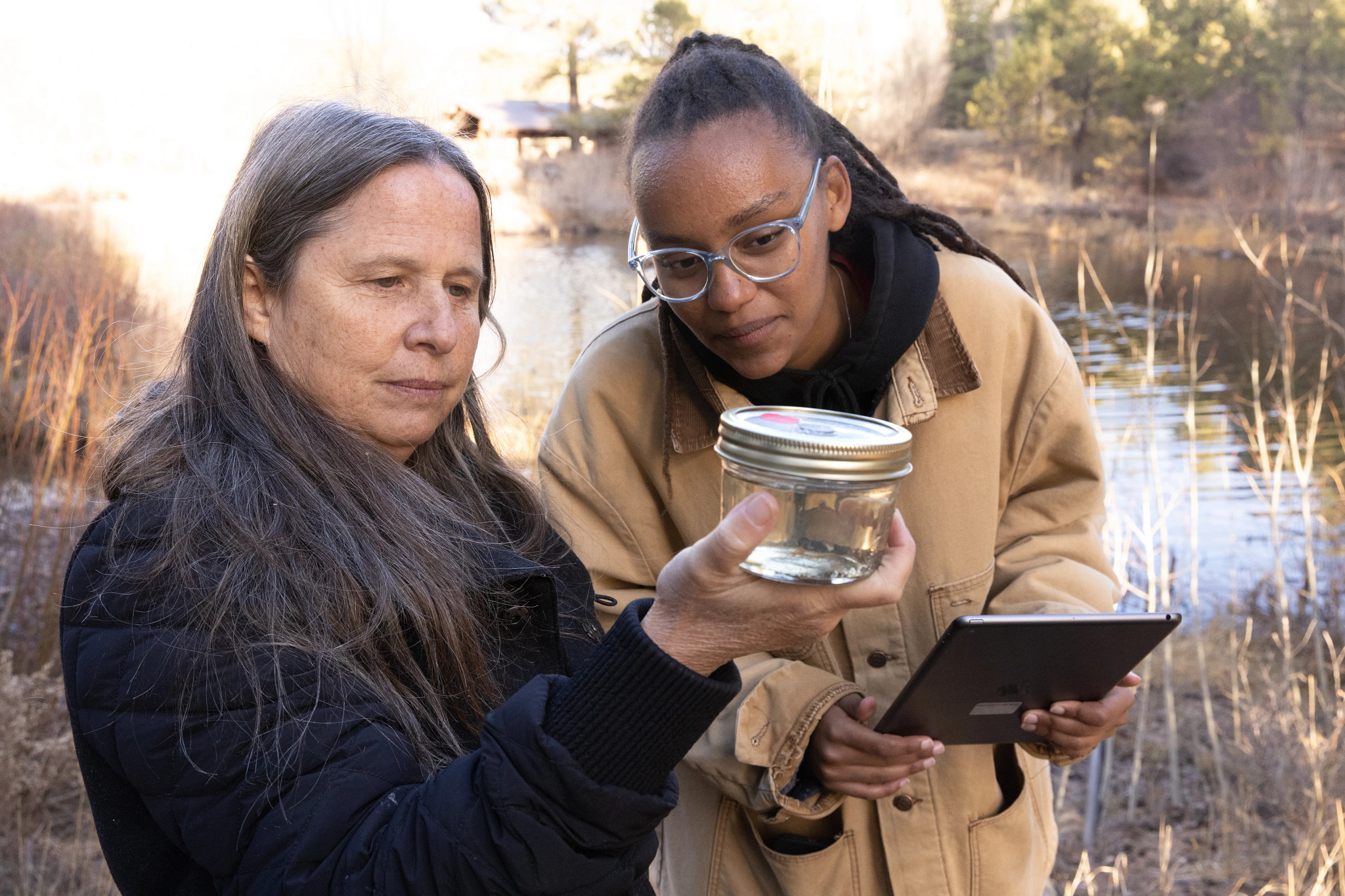 Two people studying a glass a water with specimens inside