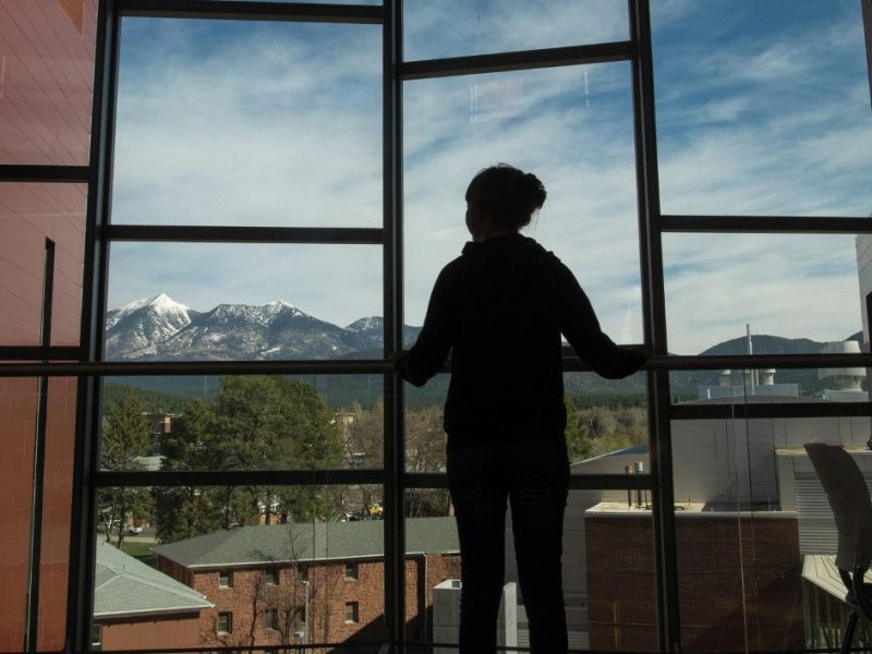 Student looking out the windows of a N A U building.