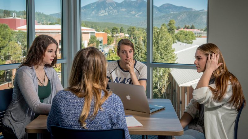 Four students sitting at a table and a computer on table.