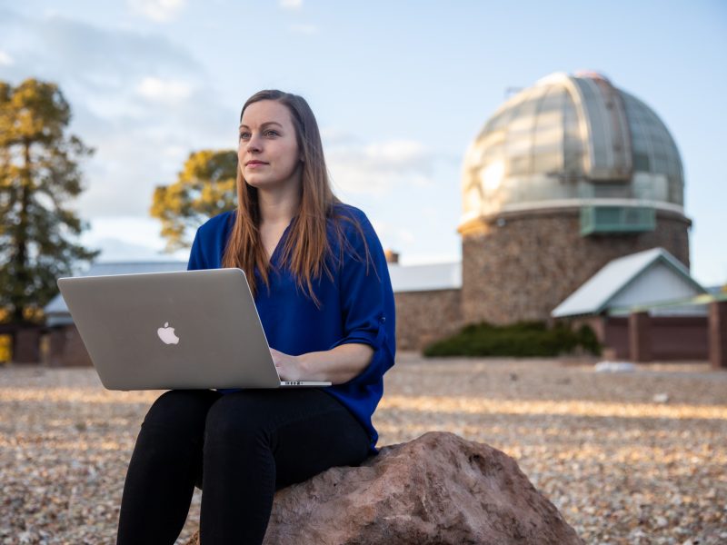 A student sitting on a rock with her computer on her lap.