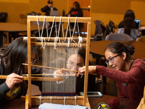 Three indigenous females learning to use a traditional loom