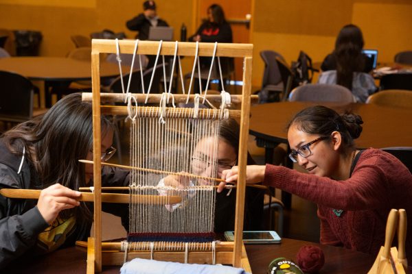 Three native students working together to use a traditional loom.