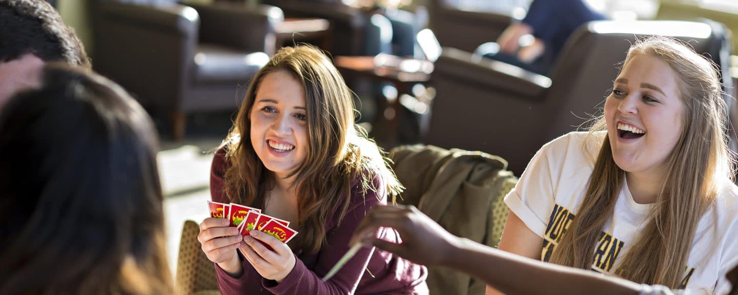 Students playing card game Apples to Apples together in lobby chairs.