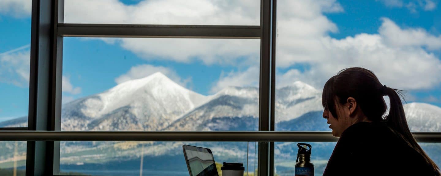 Student studying on latop with scenic mountain visible in window.