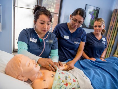 Nursing students at NAU are practicing on a manikin lying in a hospital bed.