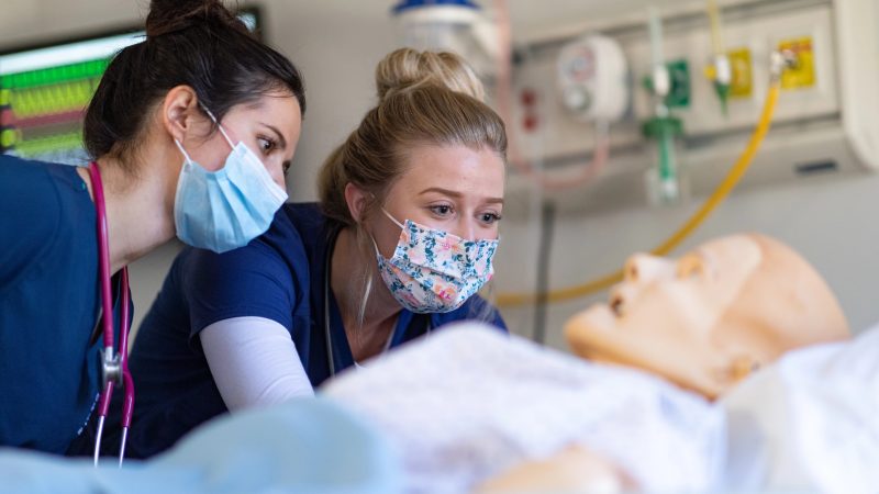 Two N A U Nursing students practice on a mannequin.