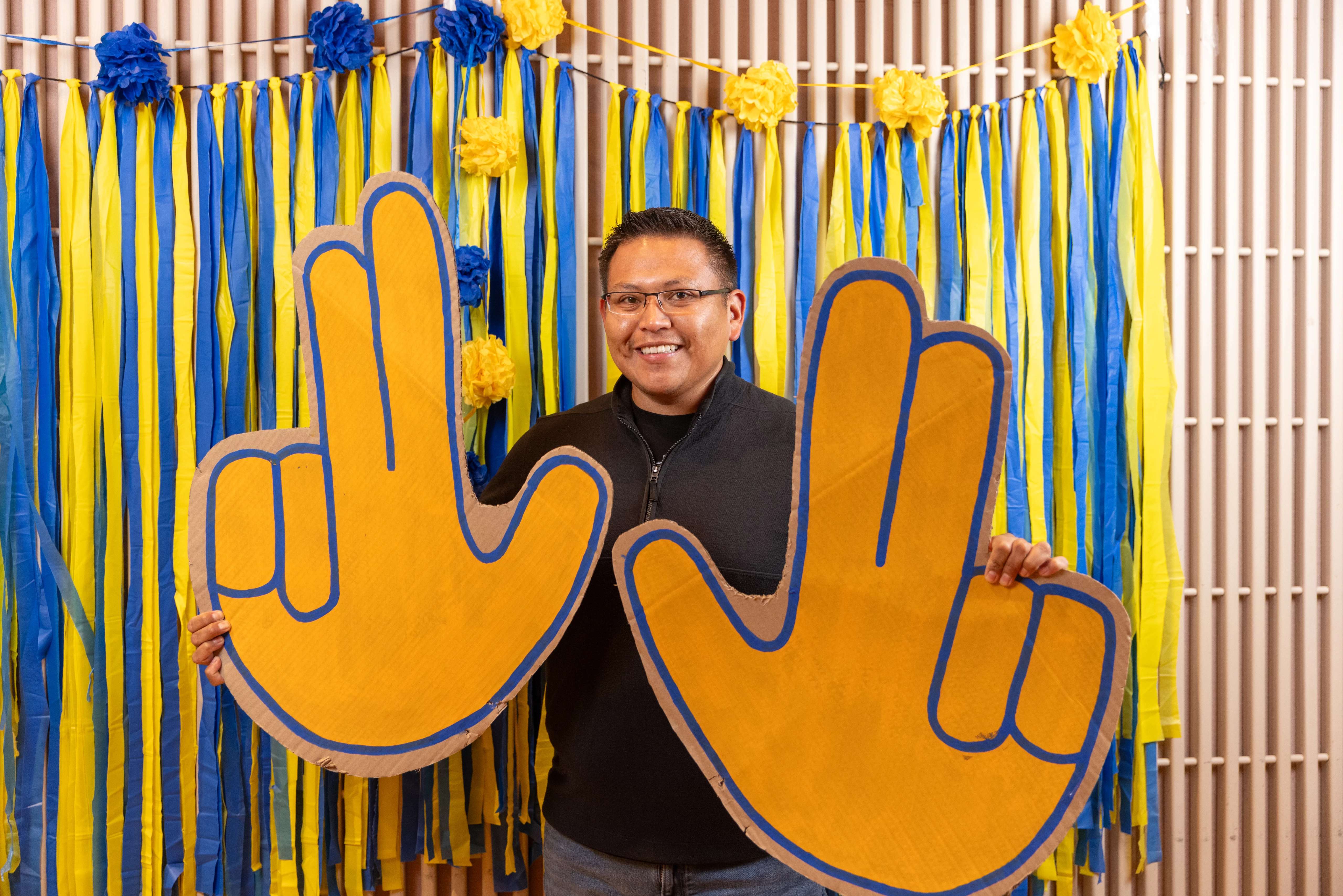 An attendee of the N A U Council of Indigenous Ambassadors showcase posing with jacks symbol props and yellow and blue streamers.