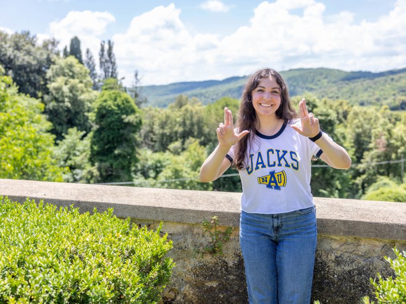 A student wearing a N A U shirt does the Lumberjacks hand symbol.