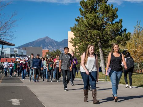 students walk along the sidewalk on NAU's campus with mountains in the background