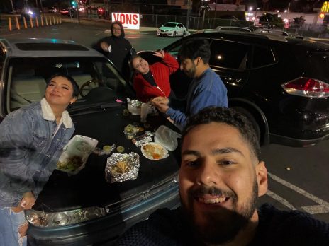Four individuals eating Mexican food on the hood of their car