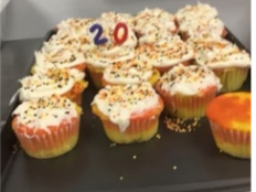 Yellow cake cupcakes with white frosting, sprinkles and candles in the shape of "20"
