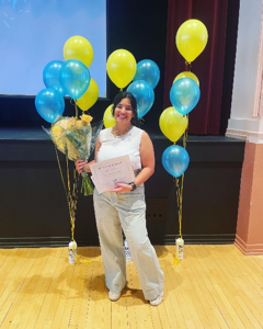 Giselle standing in front of balloons with flowers and her Graduate Service Award
