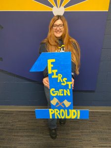 Jennifer Wadley holding a cardboard "1" with the words "First-Gen Proud" painted on it