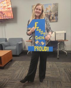Cora Brown holding a cardboard "1" with the words "First-Gen Proud" painted on it