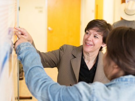 Julie Baldwin points to a poster on the wall as she works with a student researcher.