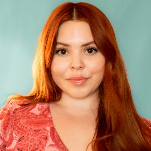 A headshot of Alexandra Olin who has red hair, and is against a blue background. 
