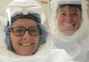 Bridget Barker poses with one of her students in a lab wearing white powered air purifying respirators.