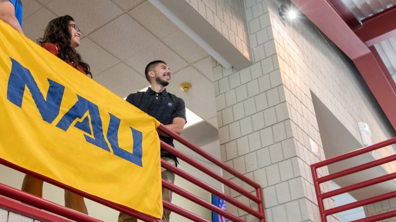Students standing and smiling next to a NAU–Yuma banner