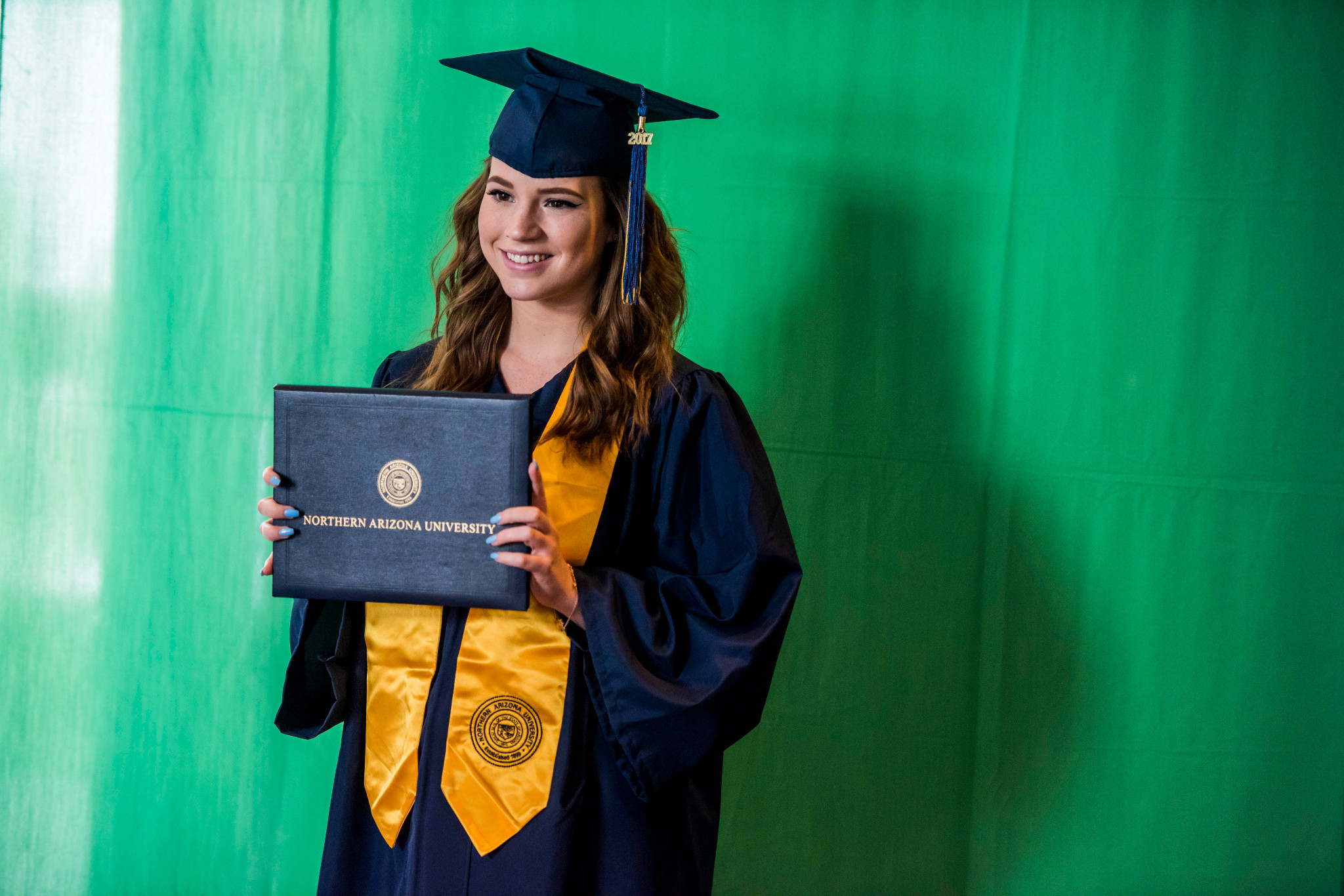 A student at NAU–Yuma holding up their diploma.