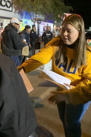 An NAU-Yuma Social Work student wearing a NAU sweatshirt hands out flyers.